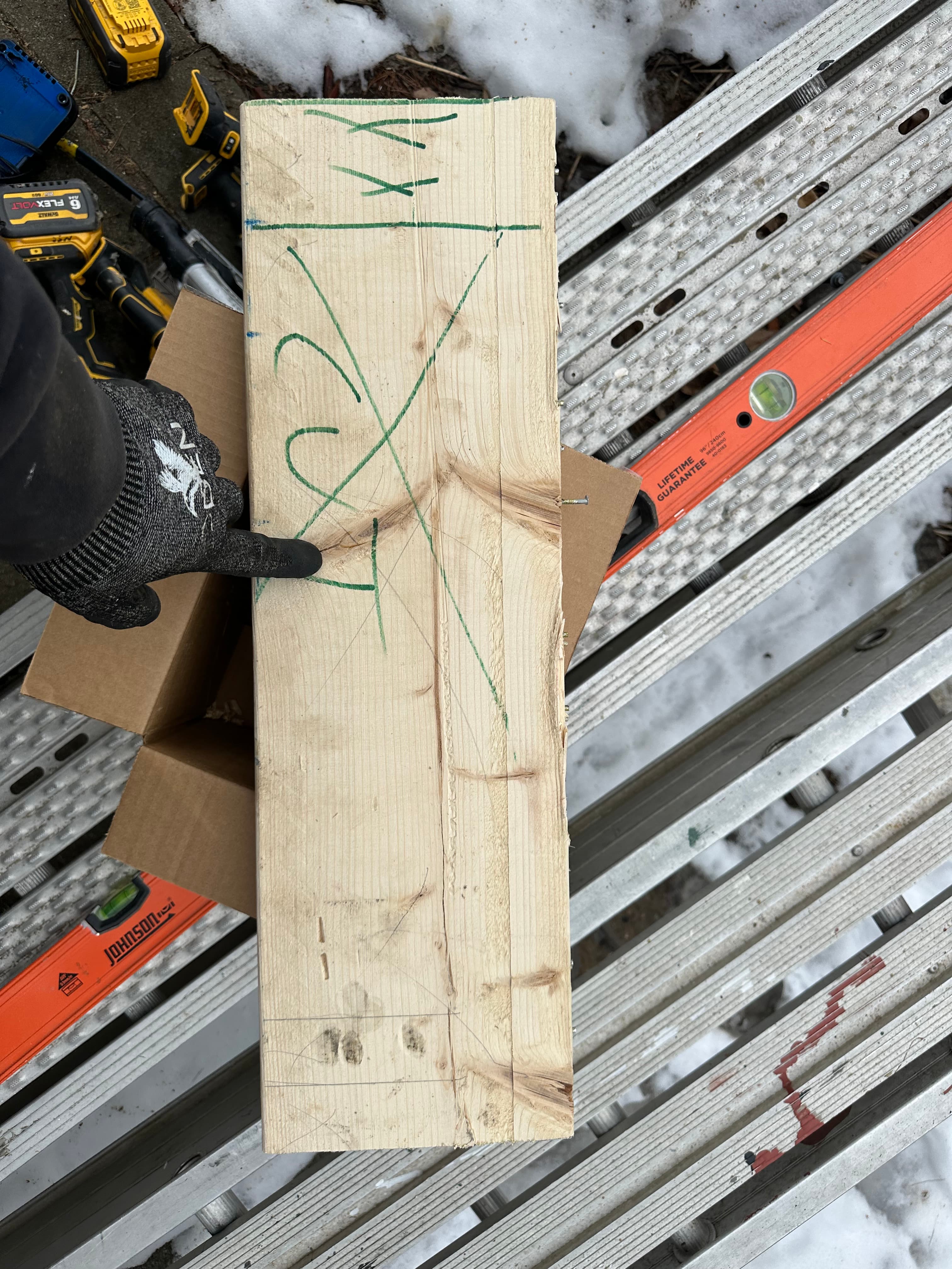 Gloved hand pointing to green markings on a wooden board resting on a metal ladder.