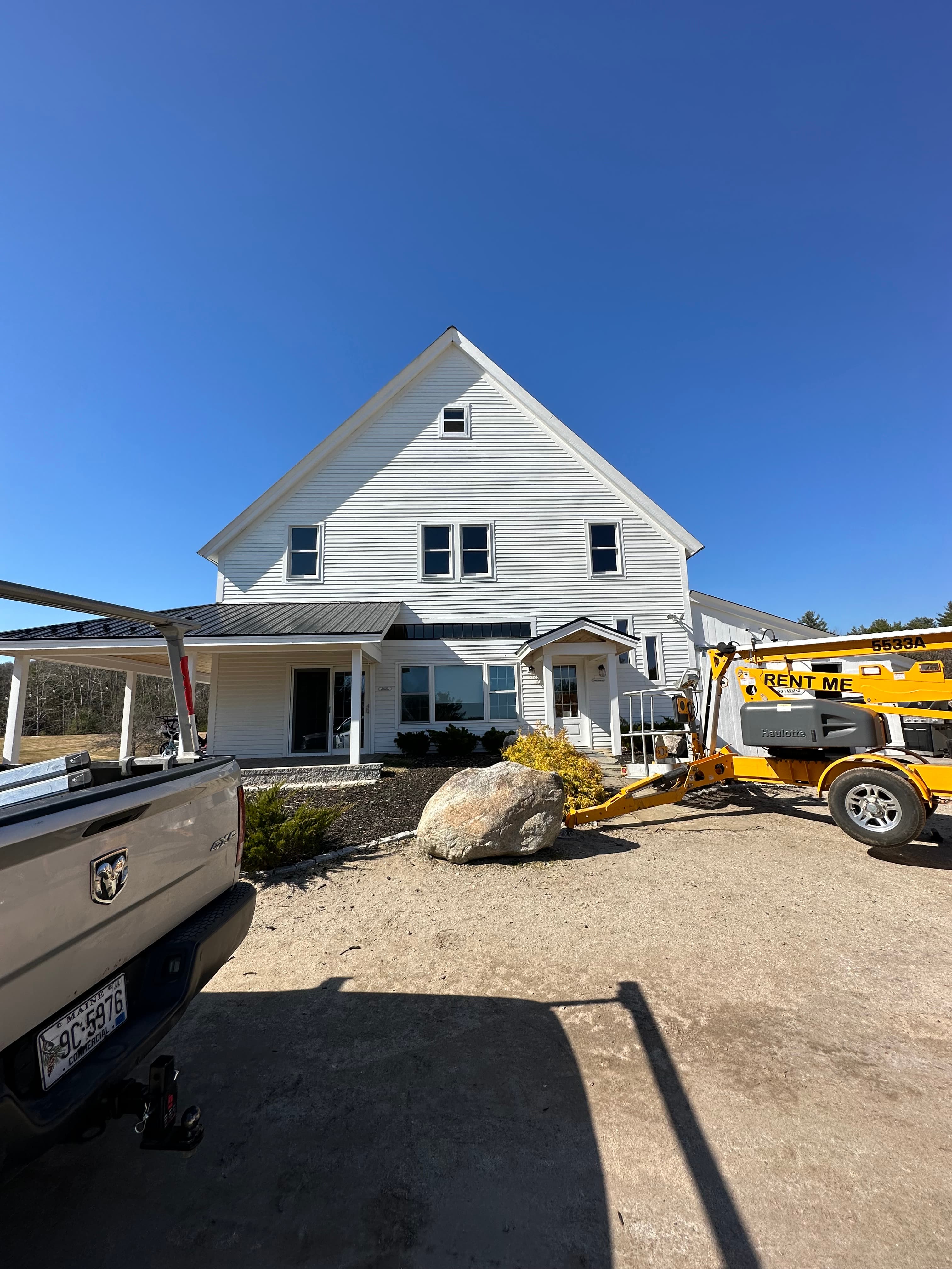 White two-story house with a silver pickup truck and yellow boom lift in the driveway.