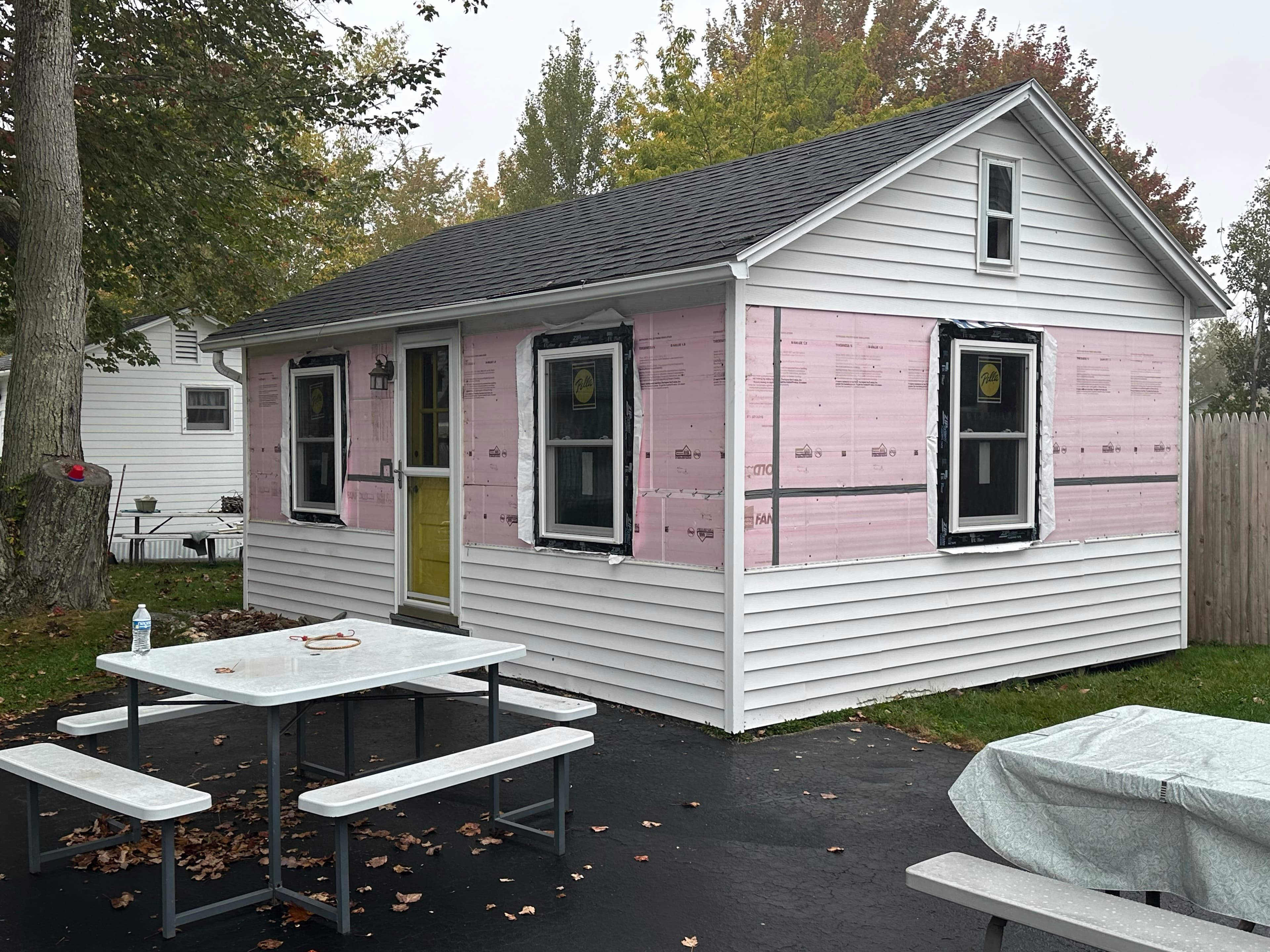 White house with pink insulation exposed during renovation, next to a white picnic table.